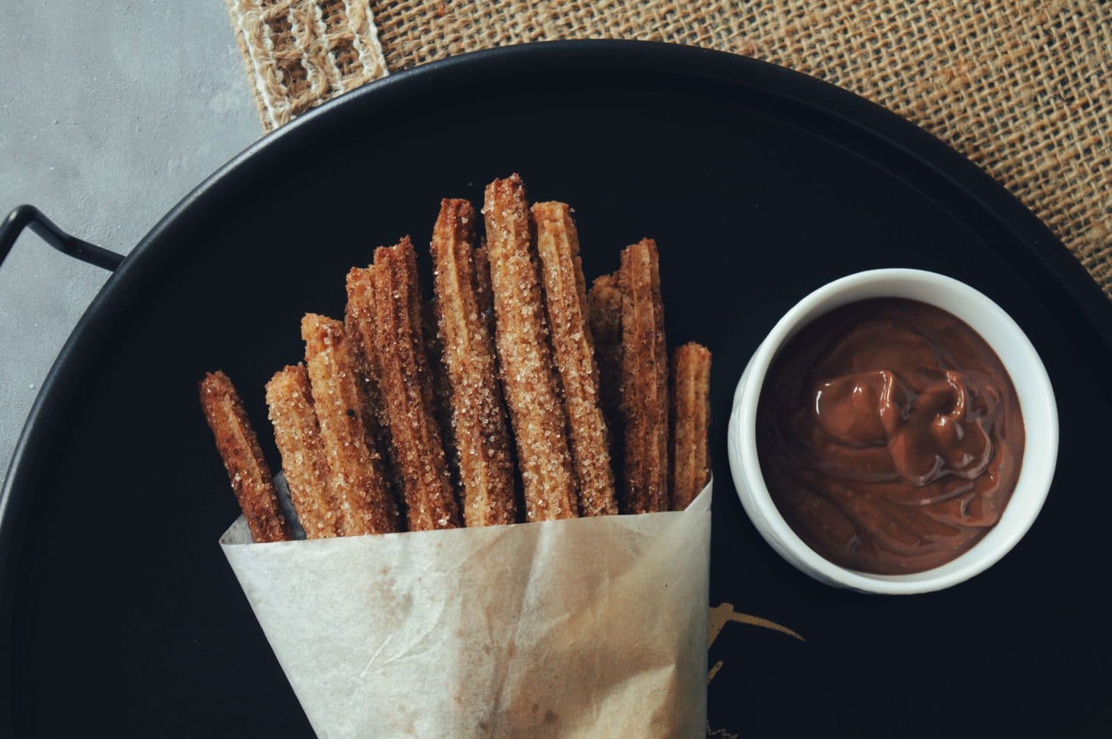 Churros in a paper cone with a bowl of hot chocolate