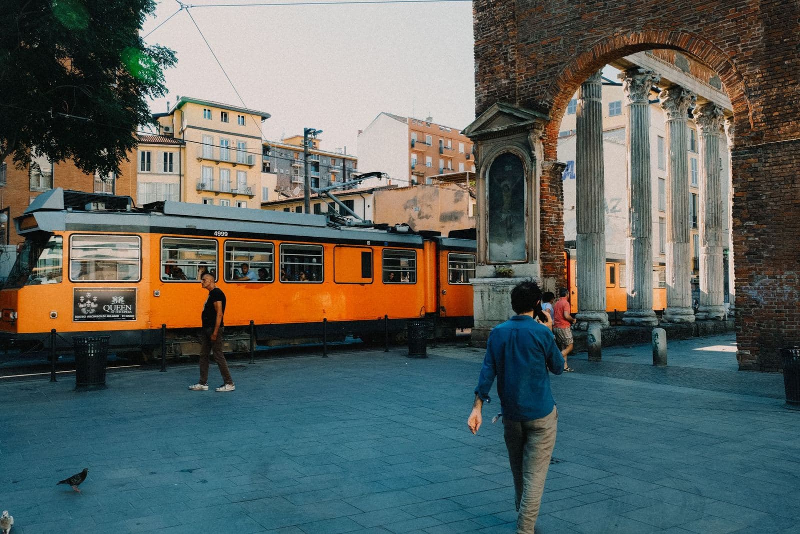 Orange tram passing the Roman columns of San Lorenzo, near the Navigli