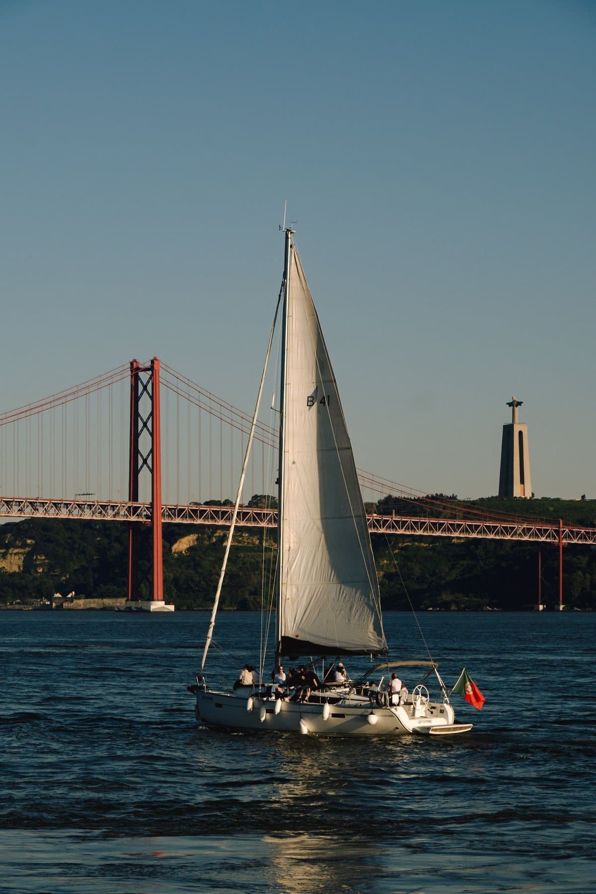 A sail passing the 25 de Abril Bridge and the Cristo Rei statue