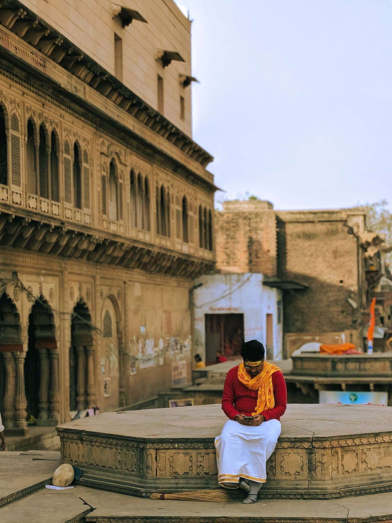 A man in traditional dress sitting outside old houses in Vrindavan