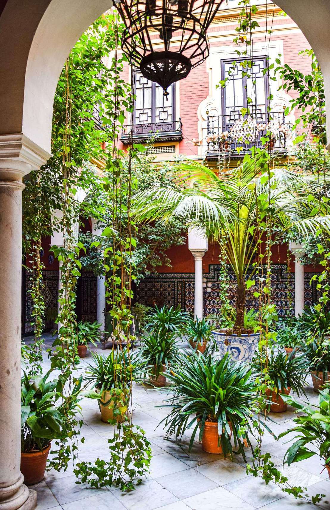 A Seville palace courtyard with palms, hanging plants and tiled walls