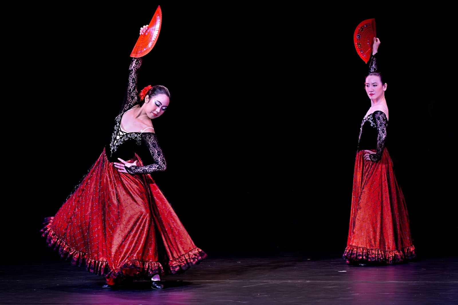 Two flamenco dancers in red and black on stage with their fans