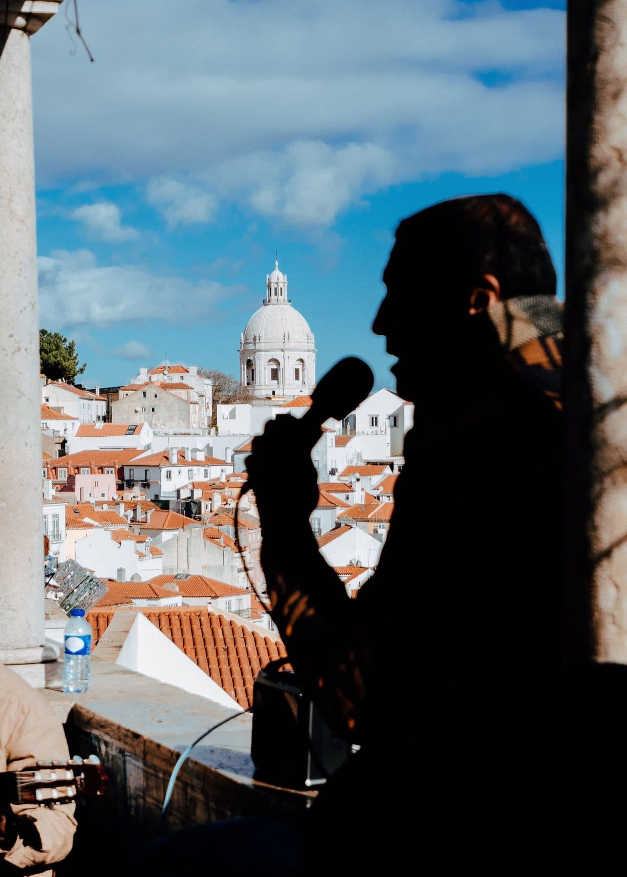 A singer in silhouette with a microphone, above Lisbon's rooftops