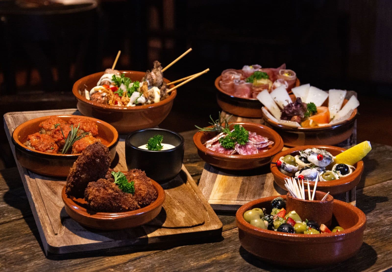 Spread of Spanish tapas in clay dishes on a wooden board