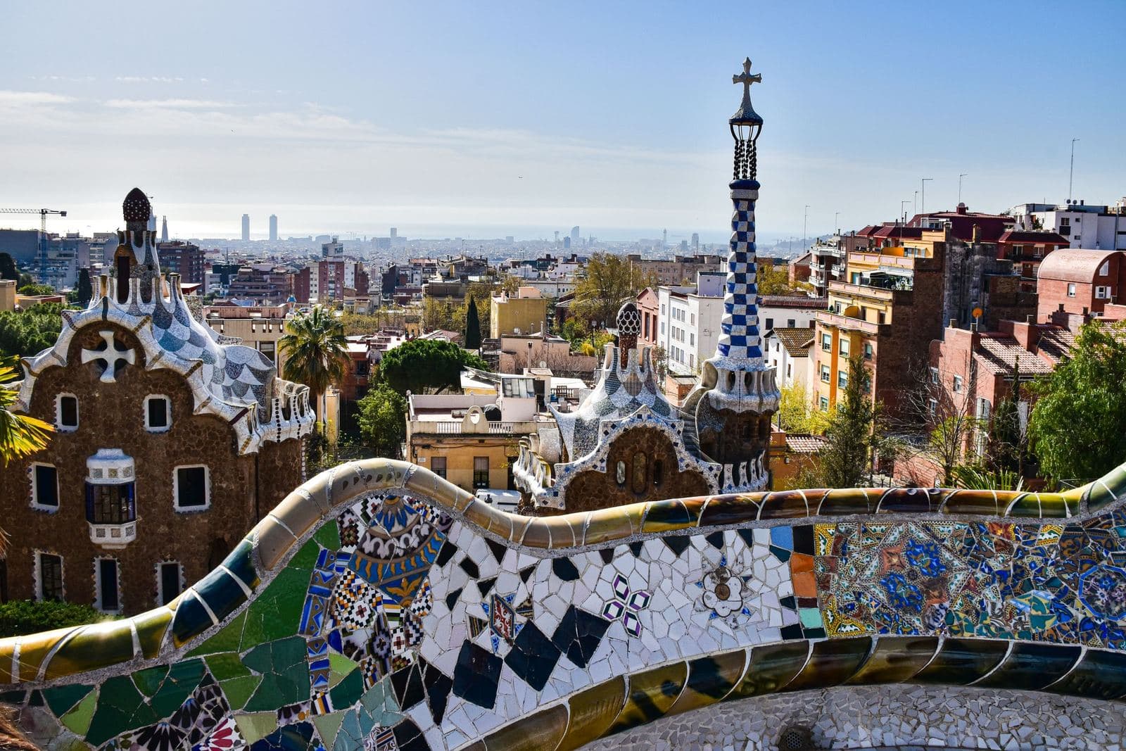 Gaudís Mosaikbank und Pförtnerhäuser im Park Güell, dahinter Barcelona