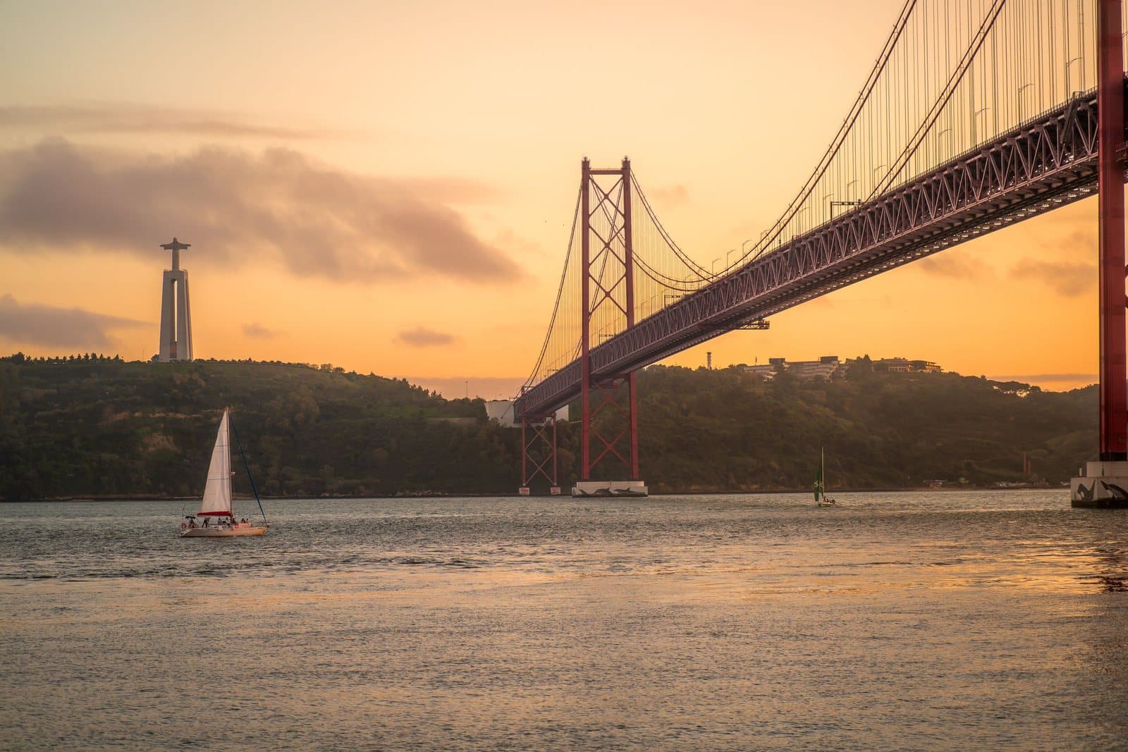 A sailboat on the Tagus at sunset below the 25 de Abril Bridge