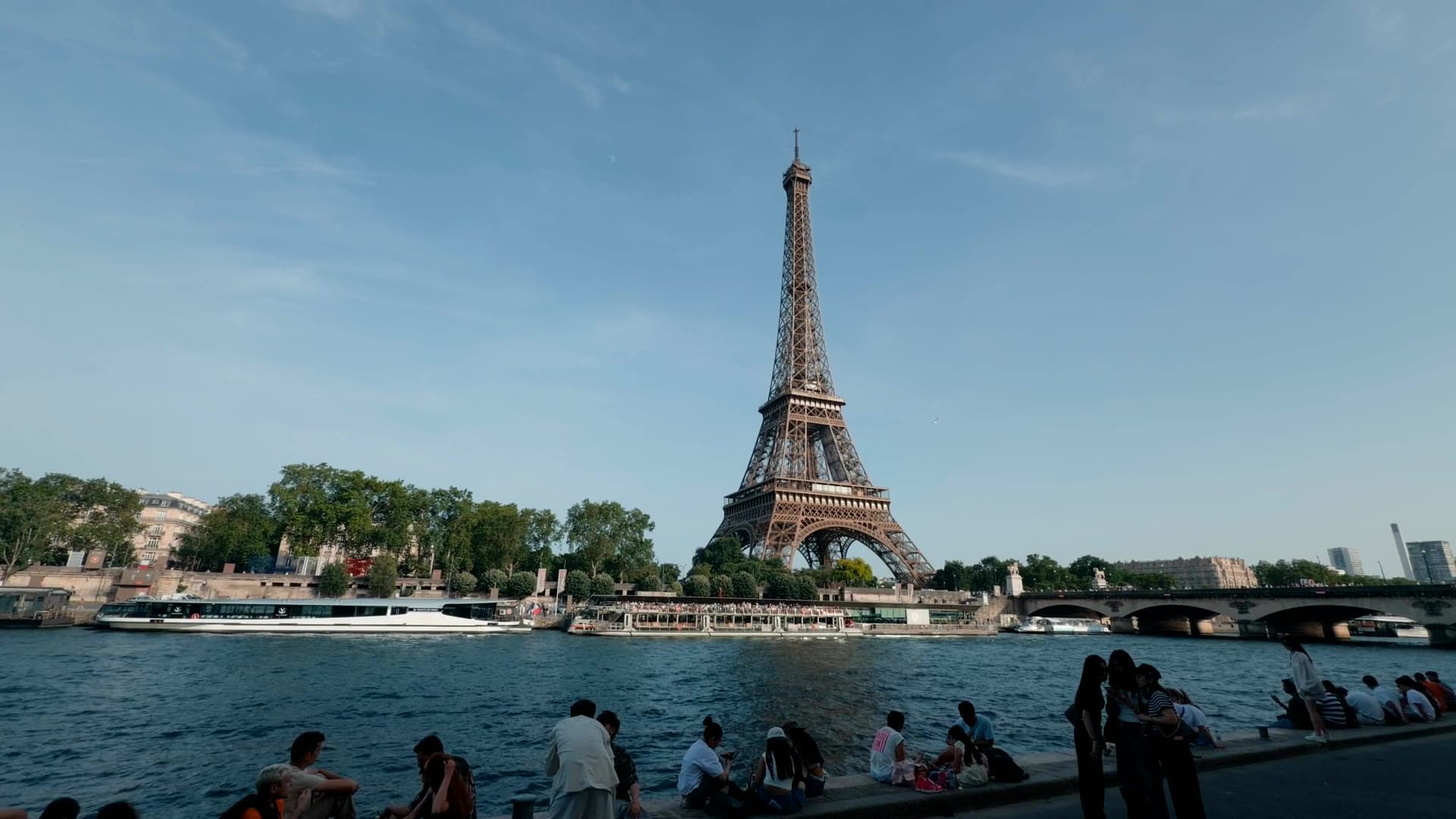 The Eiffel Tower across the Seine on a sunny day, visitors on the riverbank